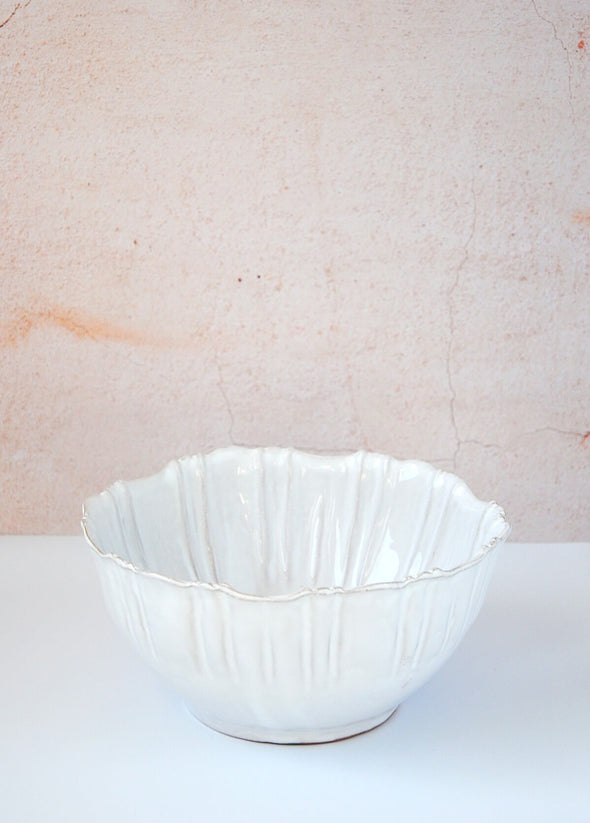 Bowl with fluted edges in a white glaze. Made from terracotta. Nine centimetres high and twenty centimetres wide.