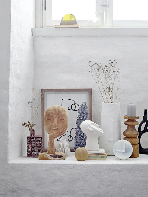Interiors shot featuring a collection of home accessories against a backdrop of white washed walls. At the back displaying some foliage is a tall white vase made from terracotta and featuring a sculpted long nose down the front. Height forty centimetres, Width seventeen centimetres.